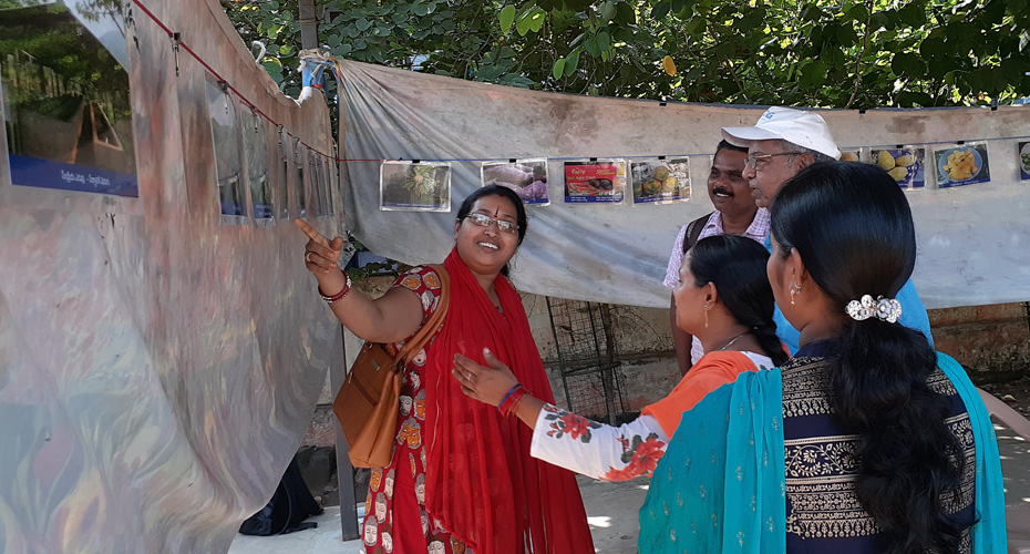 A community event in India. A woman is talking to a group of people about an exhibition about nutrition