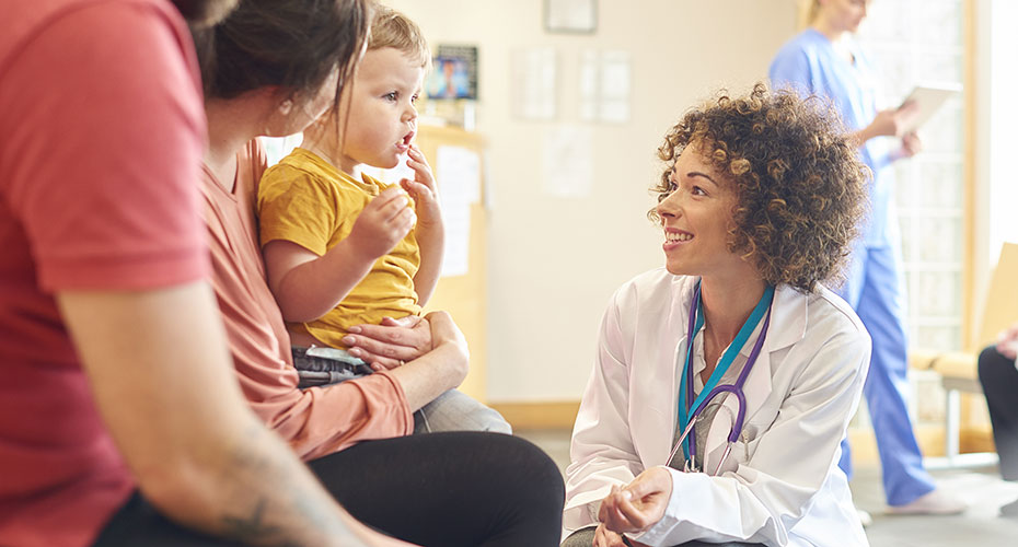 A female doctor, Crouch is down to speak to a woman with a toddler on her lap