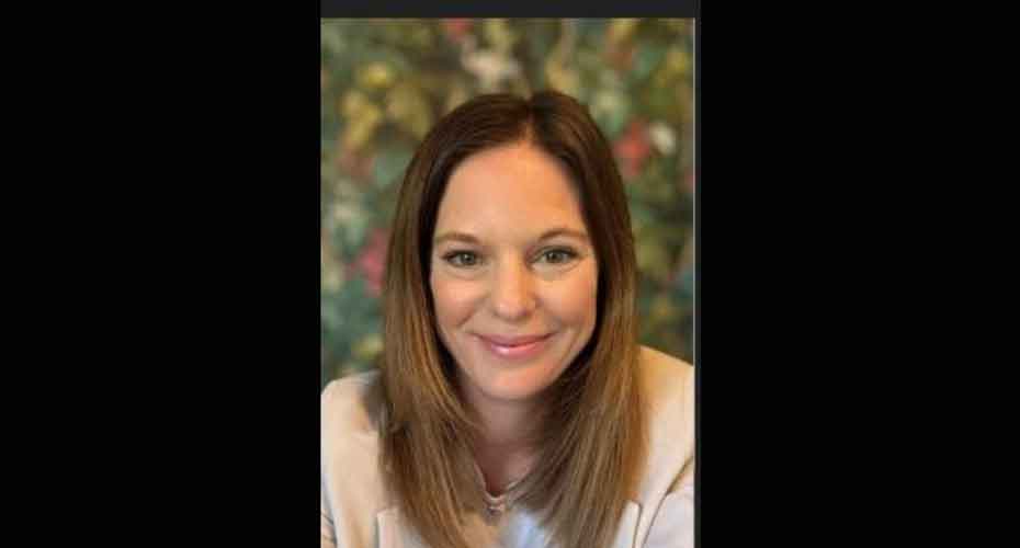Head and shoulders image of Rose Cohen smiling into camera with out of focus flower wall in background