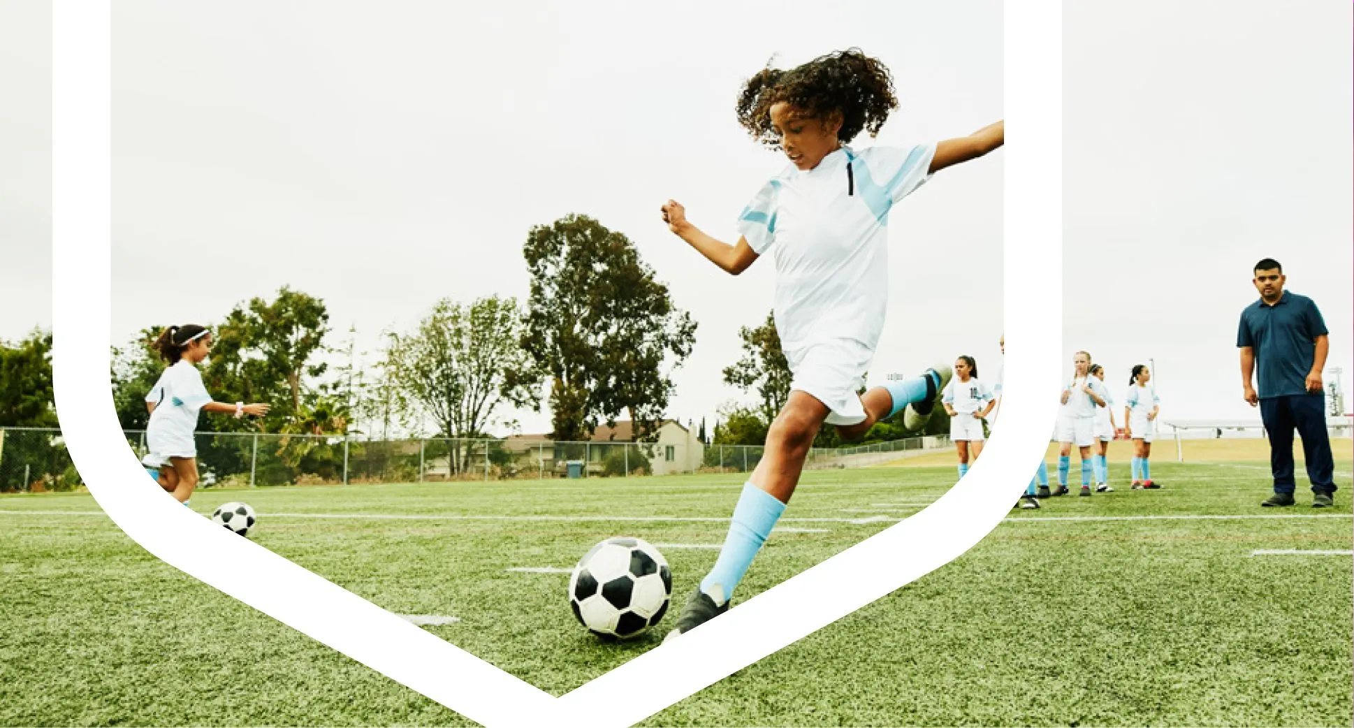 A young girl energetically kicks a soccer ball on a grassy field, showcasing her enthusiasm for the game.