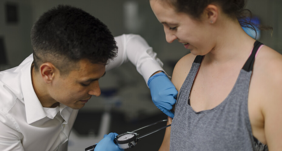 A researcher measures a colleague's body fat using calipers on her arm