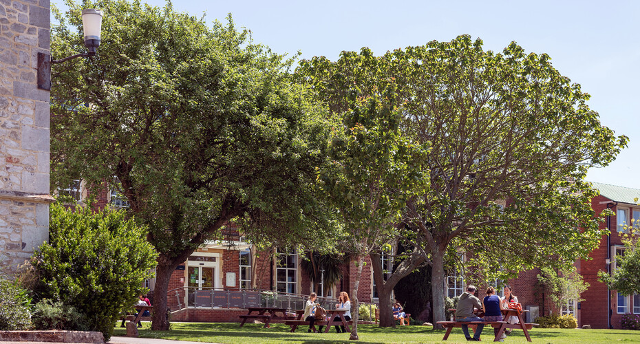 People sitting at picnic tables under trees on St Luke's Campus