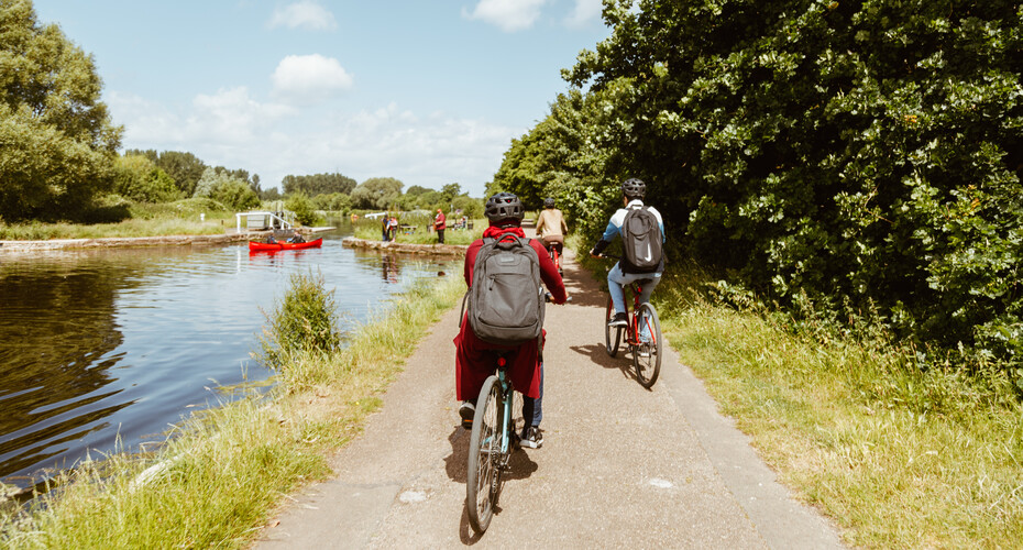 A group of young people cycling by the river, seen from behind