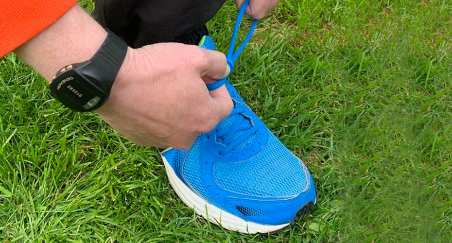 Close up on hands tying the laces of trainers. On one wrist is an accelerometer