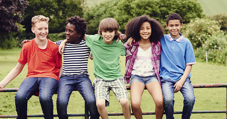 Several children of different ethnicities, sitting on a five bar gate, looking happy and healthy