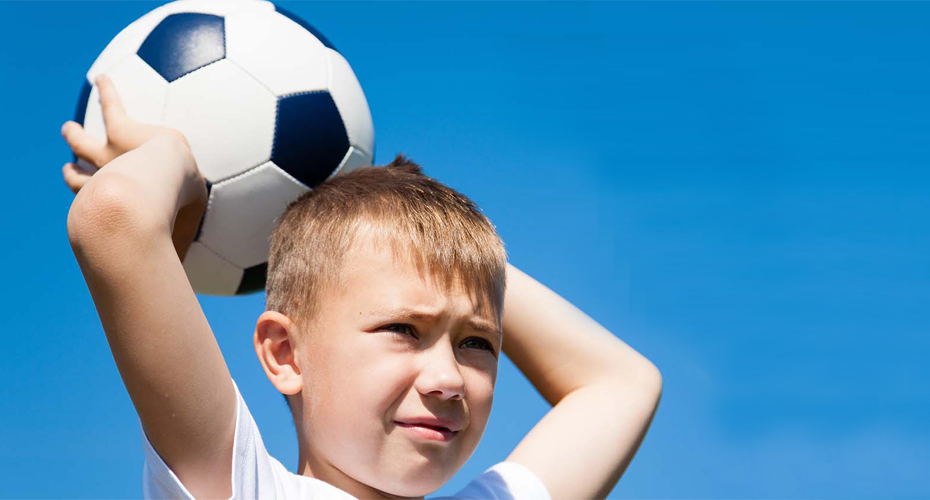 A young boy holds a football above his head. His expression is serious as he prepares to throw.