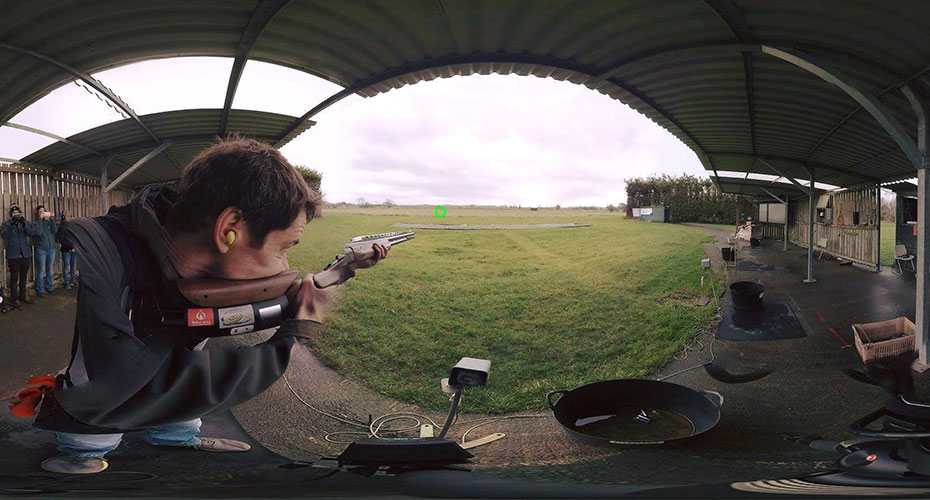 A person aiming a rifle on a rifle range, distorted through a 'fish eye' camera lens