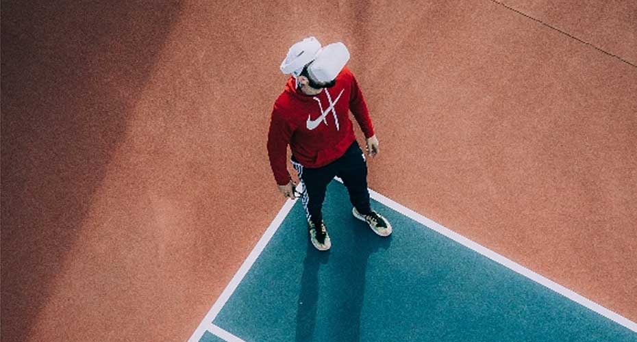Seen from above, a person standing on a tennis court wearing a VR headset
