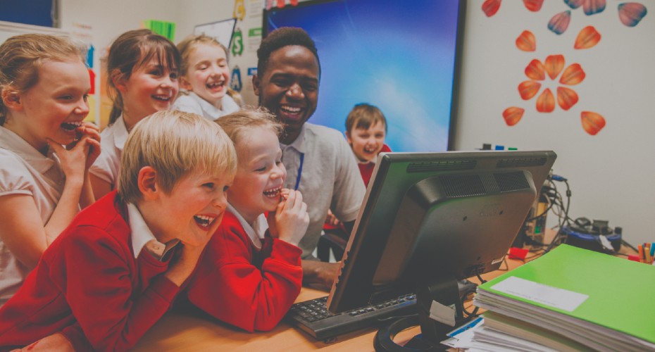 Male primary teacher with children around a computer